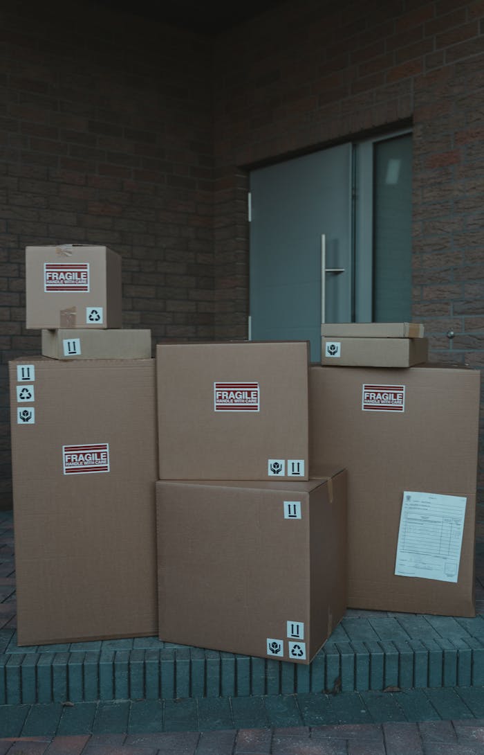who-we-are A stack of labeled cardboard boxes piled in front of a closed industrial door, symbolizing delivery service.